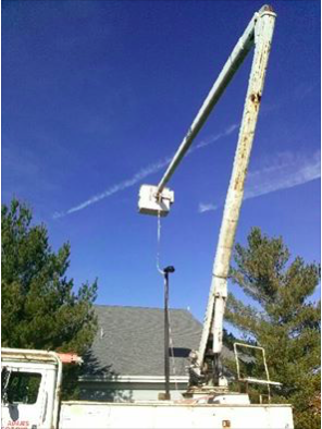 A crane is lifting a parking lot light into place.